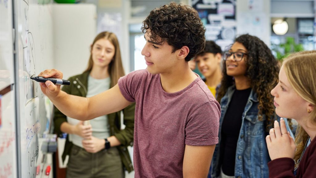 Teen Student solving math equation on whiteboard at high school