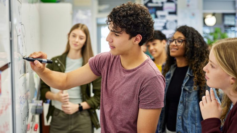 Teen Student solving math equation on whiteboard at high school