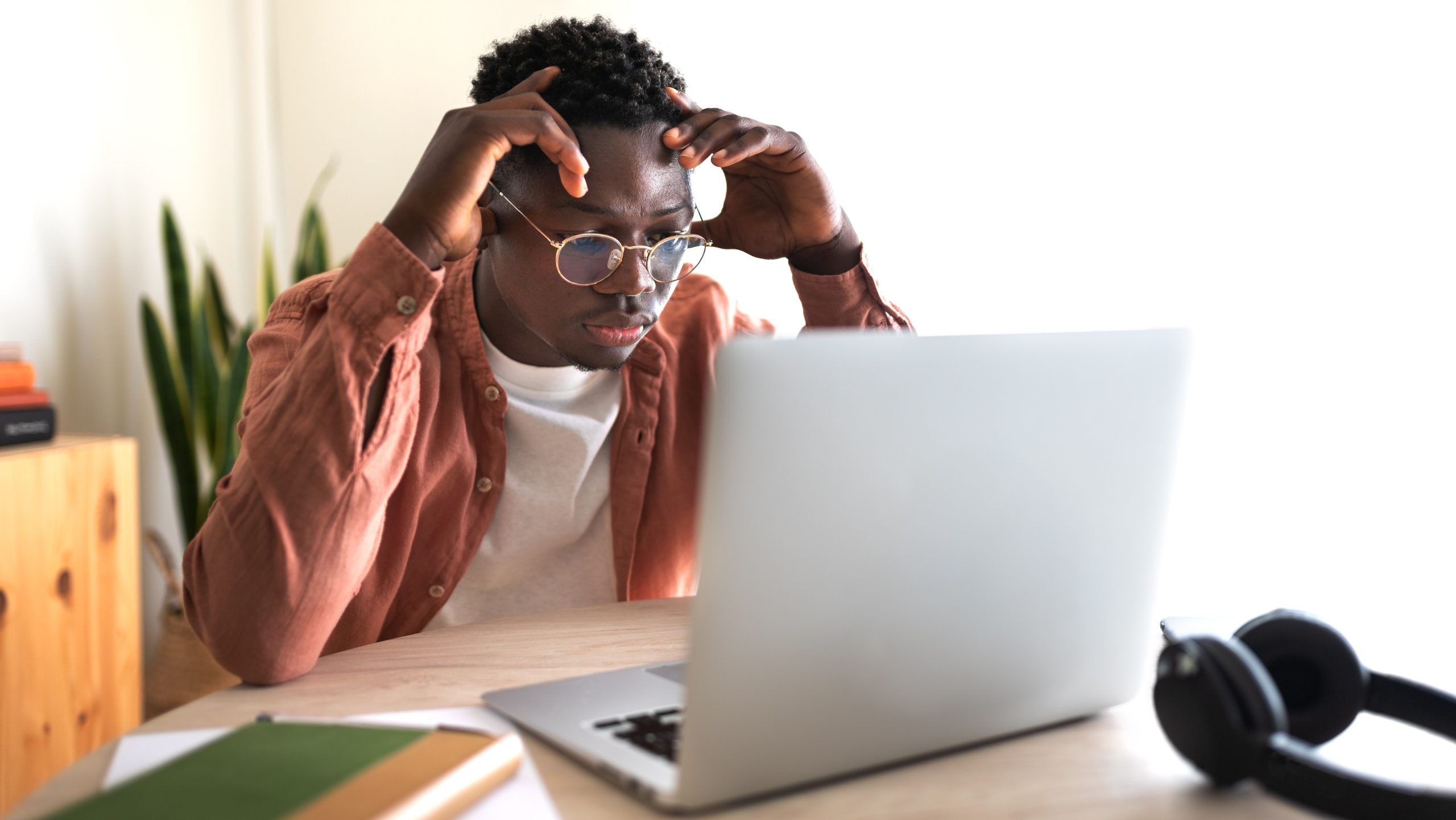 African American black male college student stressed and overwhelmed studying in front of laptop.